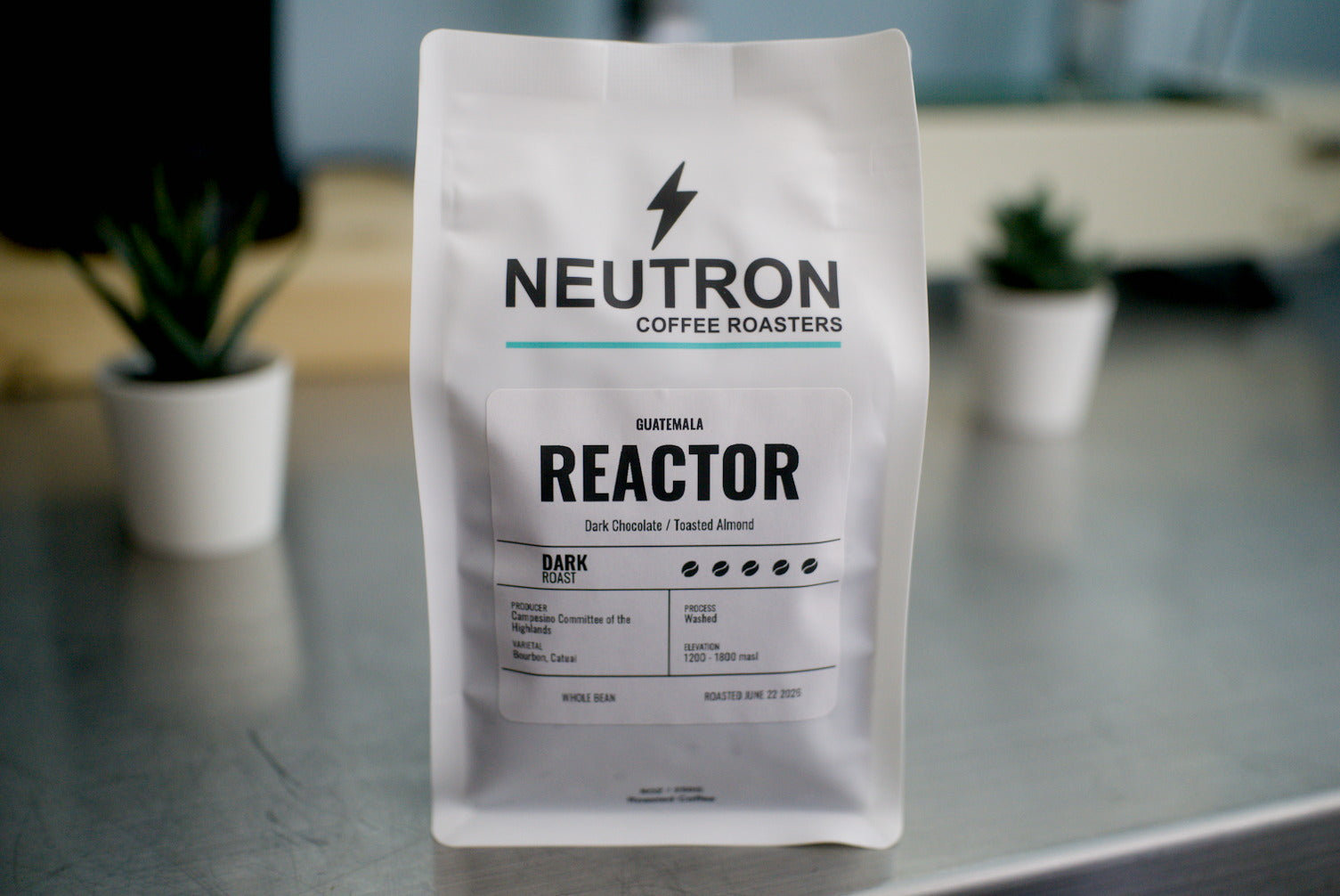 Neutron Coffee Roasters Reactor coffee bag on a metal surface with a blurred background.