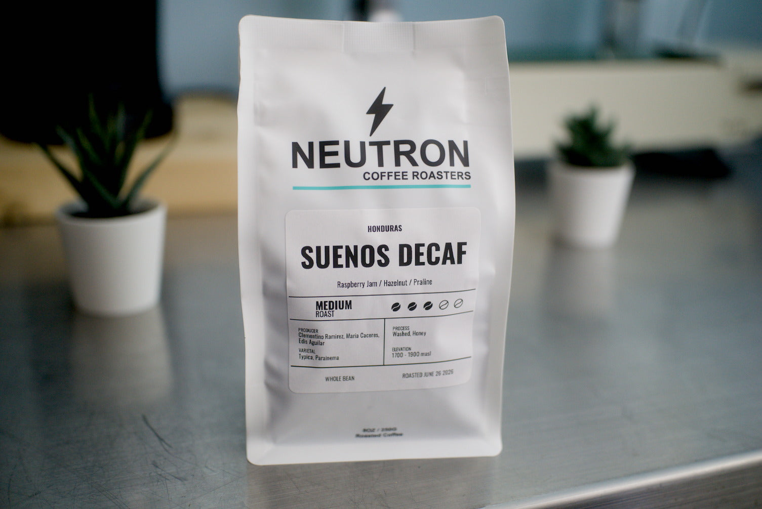 Neutron Coffee Roasters Suenos Decaf coffee bag on a metal surface with a blurred background.